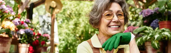 Senior woman with a warm smile relaxes in her lush garden, surrounded by blooming flowers in pots. — Stock Photo