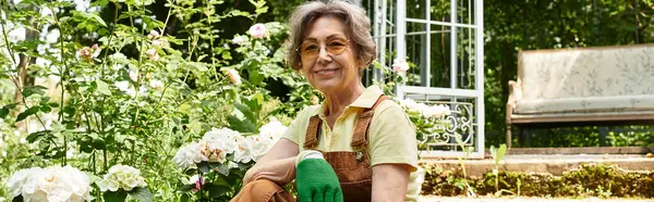 A lovely senior woman cares for her vibrant garden filled with blooming flowers and sunlight. — стокове фото