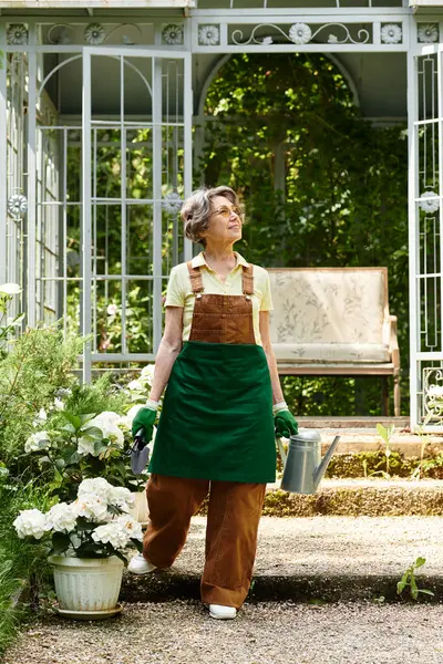 Beautiful senior woman walks through her lush garden, nurturing flowers with a watering can. — стокове фото