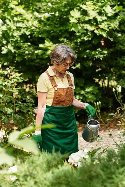 Beautiful senior woman in a lush garden carefully watering her flowers while enjoying nature. — Stock Photo