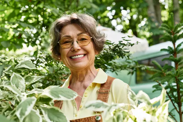 Senior woman smiles brightly while nurturing her vibrant garden filled with greenery and life. — Stock Photo