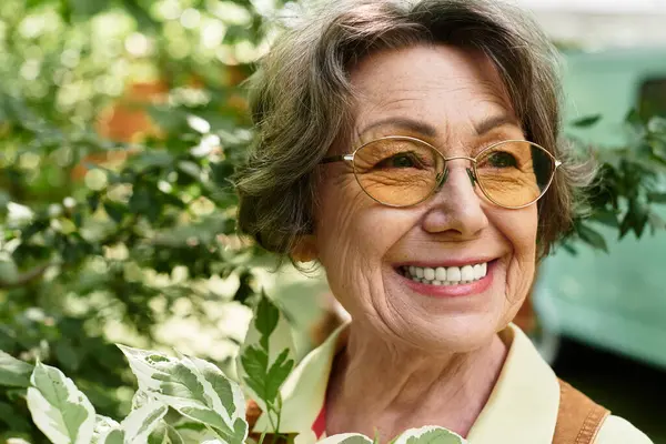 A smiling senior woman is surrounded by fragrant flowers and greenery in her garden. — стокове фото
