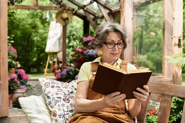 Senior woman enjoys a peaceful moment reading surrounded by vibrant flowers in the garden. — Stock Photo