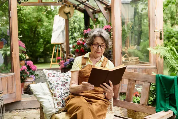 In a serene garden, a lovely senior woman enjoys a book amid vibrant flowers. — Stock Photo
