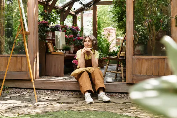 Beautiful senior woman sits peacefully in a garden, surrounded by blooming flowers and greenery. — стокове фото
