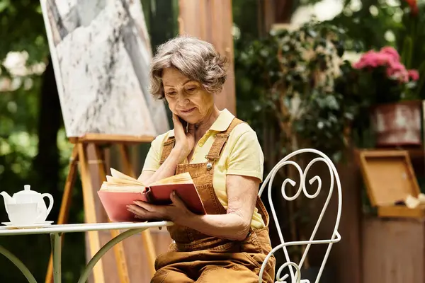 A lovely senior woman reads a book in a charming garden filled with greenery and blossoms. — Stock Photo