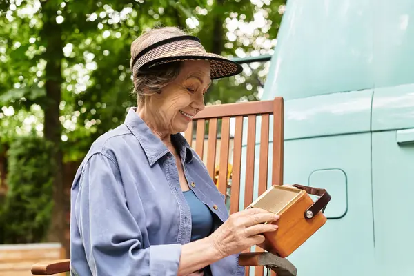 A senior woman smiles as she carefully examines a wooden box surrounded by blooming flowers. — Stock Photo