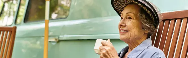 Bright sunlight filters through garden trees as a senior woman sips coffee, smiling contentedly. — стокове фото