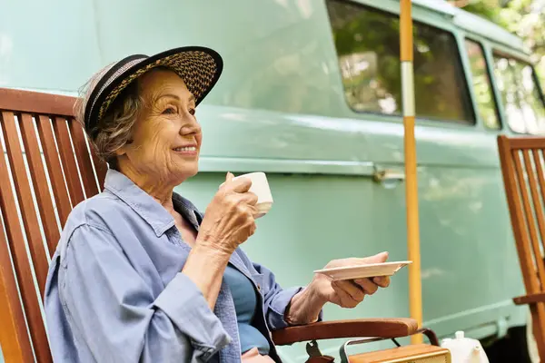Beautiful senior woman relaxes in a garden, savoring tea while sitting in a comfortable chair. — Stock Photo
