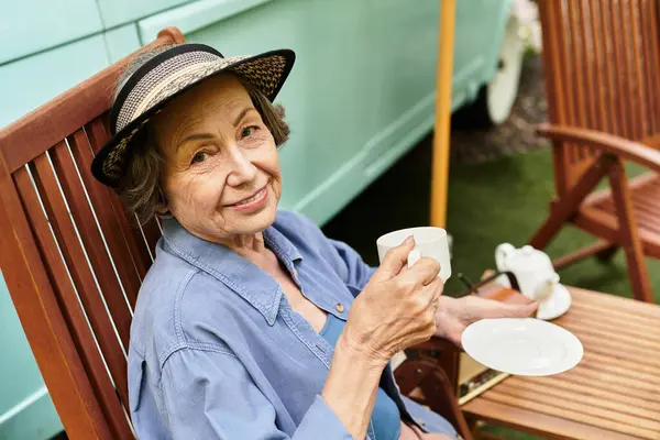 A joyful senior woman relaxes in her colorful garden, sipping tea and enjoying the tranquility. — Stock Photo