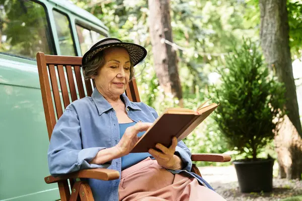 A senior woman relaxes in a garden chair, absorbed in a book, surrounded by natures beauty. — стокове фото