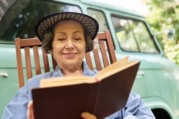 In a tranquil garden, a senior woman relaxes on a chair, engrossed in her book, radiating happiness. — Stock Photo