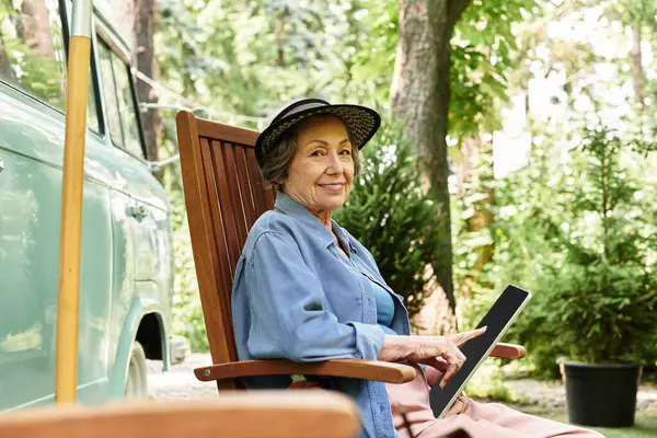 Beautiful senior woman relaxes in her garden, engaging with her tablet while surrounded by greenery — Stock Photo