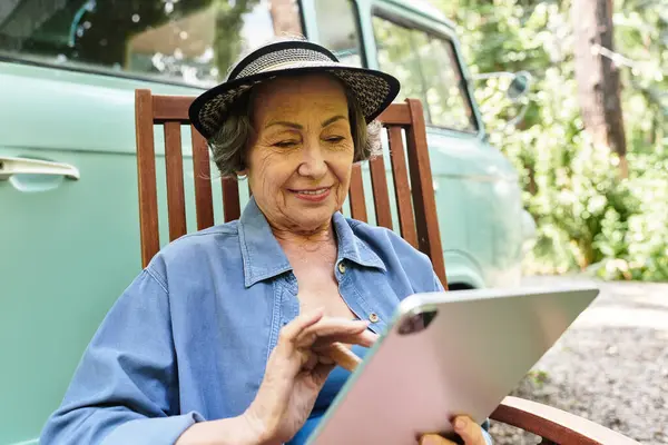 Senior woman relaxes in garden with a tablet, appreciating natures tranquility and beauty. — Stock Photo