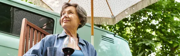 A beautiful senior woman relaxes in a lush garden under a charming umbrella, savoring her wine. — Stock Photo