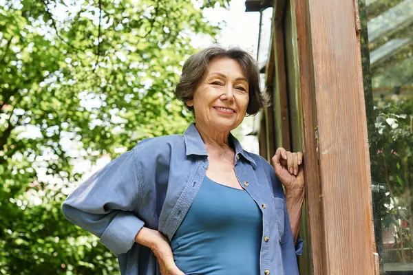 A senior woman stands happily in her garden, basking in the sunlight and surrounded by lush plants. — Stock Photo