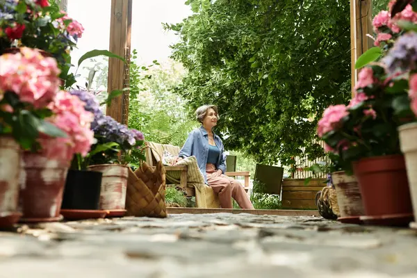 Senior woman relaxes on a bench in a sunny garden of colorful blooming flowers. — Stock Photo