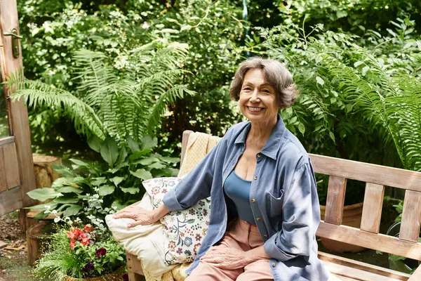 A senior woman relaxes on a wooden bench in a picturesque garden filled with plants and flowers. — стокове фото