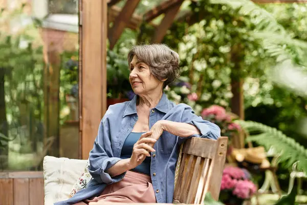 A beautiful senior woman relaxes in a lush garden, surrounded by colorful blooms and greenery. — стокове фото