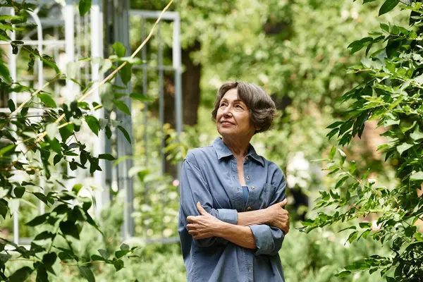 A senior woman stands gracefully in a lush garden, absorbing the serene beauty around her. — Stock Photo