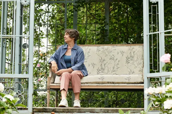 Senior woman relaxes on a garden bench, appreciating the beauty of her blooming oasis in spring. — стокове фото