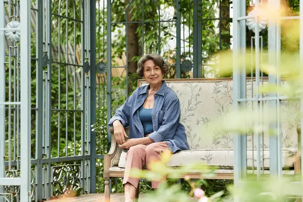 A senior woman relaxes in her garden, surrounded by lush greenery and colorful flowers. — стоковое фото