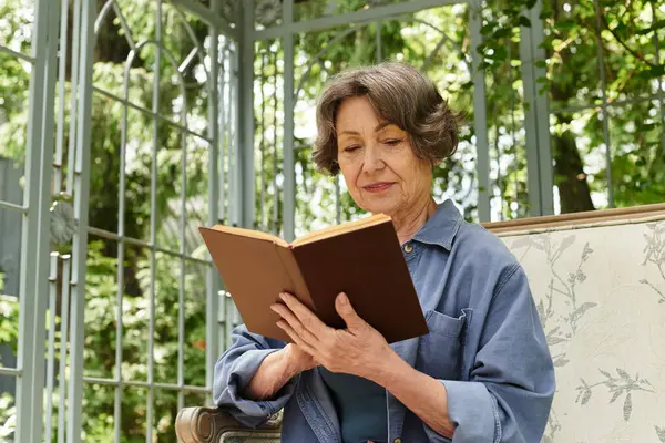 An elegant senior woman finds joy in reading a book among the greenery of a vibrant garden. — стокове фото