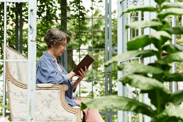 An elderly woman relaxes in an armchair, reading a book in a peaceful garden. — Stock Photo