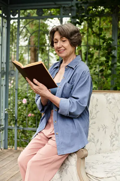 A serene senior woman reads a book in a lush garden. — Stock Photo