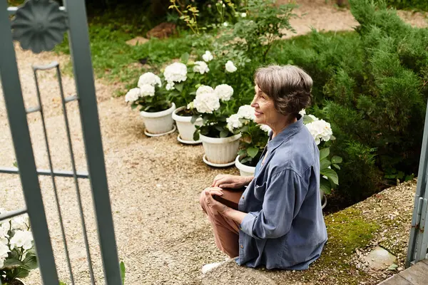 A senior woman smiles while sitting in a tranquil garden surrounded by blooming flowers. — Stock Photo