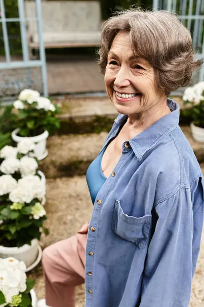 A joyful senior woman stands among blooming flowers in her garden, radiating happiness and peace. — Stock Photo