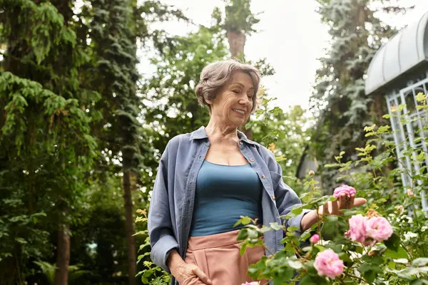 Senior woman admires blooming roses while enjoying the tranquility of her lovely garden. — стоковое фото