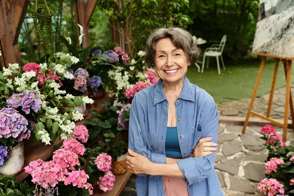 A joyful senior woman smiles amid vibrant flowers in a lively garden. — Stock Photo