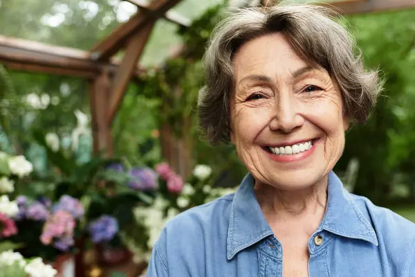 A cheerful senior woman tends her vibrant garden of blooming flowers. — стокове фото
