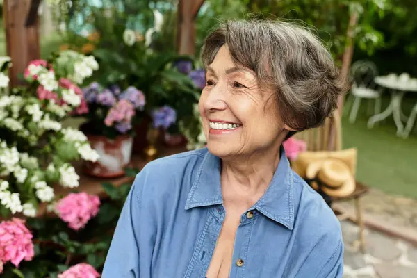 A senior woman smiles brightly while surrounded by colorful flowers in a lush garden setting. — Stock Photo