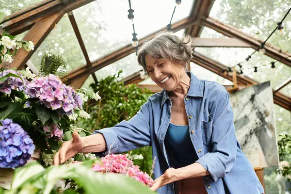 Senior woman smiles brightly while caring for colorful flowers in a lush garden during daytime. — стокове фото