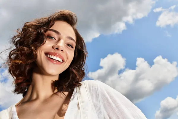 A young woman with wavy brown hair smiles outdoors on a sunny day with a blue sky. — Stock Photo