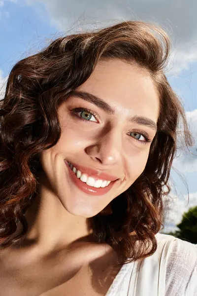 Wavy brown-haired woman smiles brightly under a clear blue sky on a warm summer day. — Stock Photo