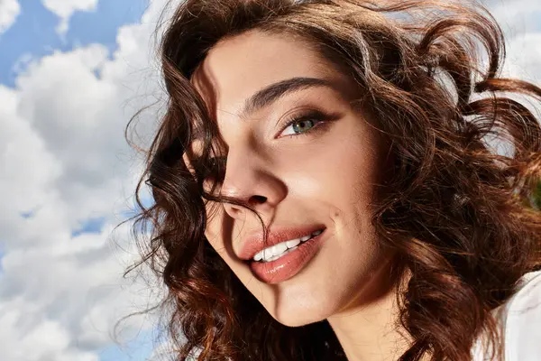 Wavy brown-haired woman smiles against a vivid blue sky on a sunny summer day outdoors. — Stock Photo