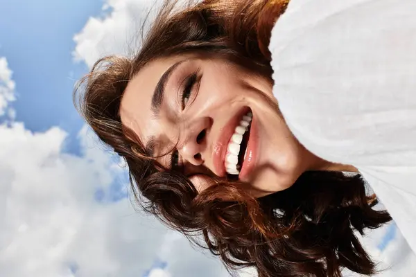 A young woman with wavy brown hair enjoys a joyful summer day under a clear blue sky. — Stock Photo