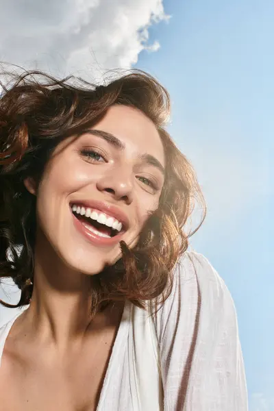 On a sunny summer day, a young woman with wavy brown hair smiles joyfully while standing outdoors. — Stock Photo