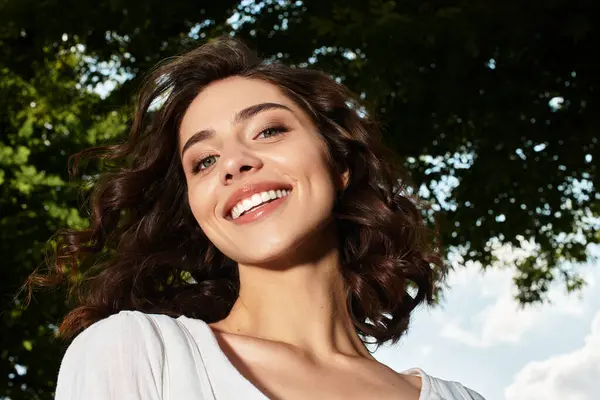 A pretty young woman with wavy brown hair enjoys a sunny day in the park, radiating joy. — Stock Photo