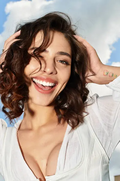 A pretty young woman enjoys a sunny day outdoors, showcasing her wavy brown hair and radiant smile. — Stock Photo