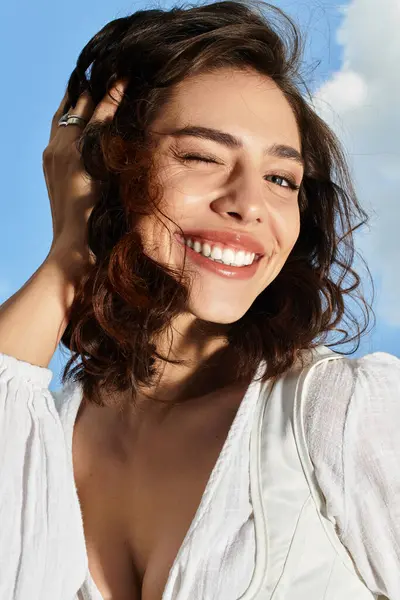 A cheerful young woman with wavy brown hair smiles while enjoying a sunny summer day outside. — Stock Photo