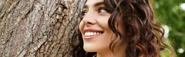 Wavy brown-haired woman smiles warmly in a sunny park, embracing the joy of summer outdoors, banner — Stock Photo