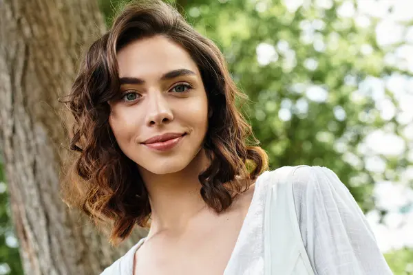 Bright summer day finds a joyful young woman with wavy brown hair relaxing in a serene park. — Stock Photo