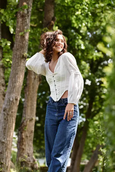 Wavy haired woman smiles while standing amid trees on a beautiful summer day in the park. — Stock Photo