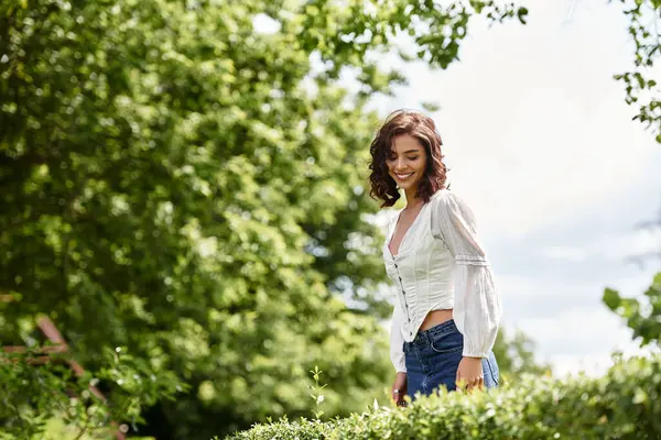 Young woman with wavy brown hair smiles while exploring a beautiful park on a sunny day. — Stock Photo