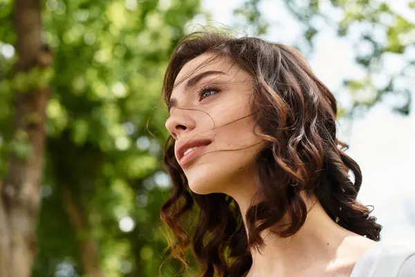 Bright sunlight illuminates a pretty young woman with wavy brown hair as she enjoys nature outdoors. — Stock Photo