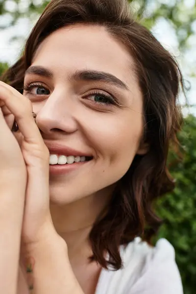A pretty young woman enjoys a sunny summer day, smiling in a lush green park setting. — Stock Photo